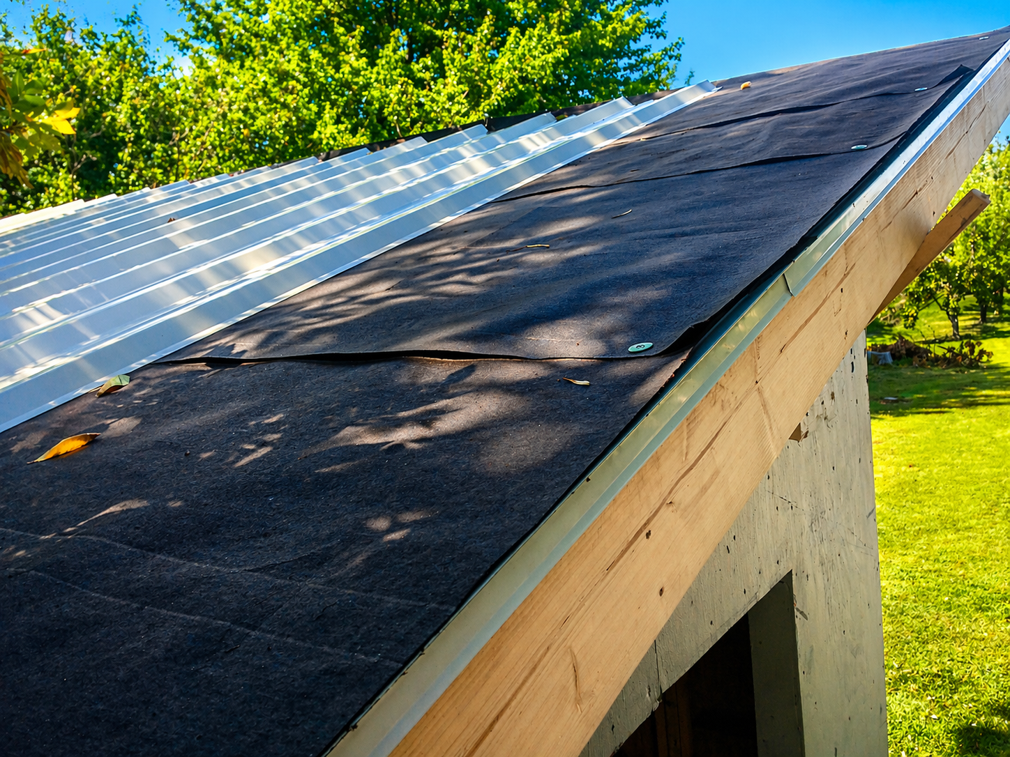 Roof with felt rolled out and metal roofing panels being installed