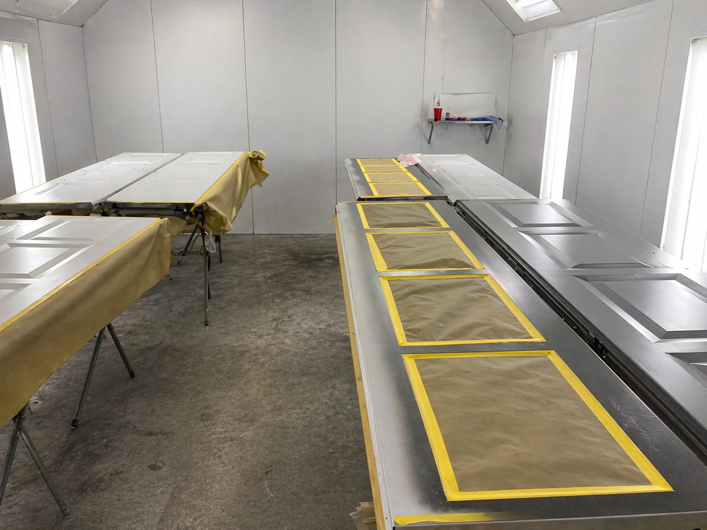 Two long garage door panels in a paint booth masked for spray painting