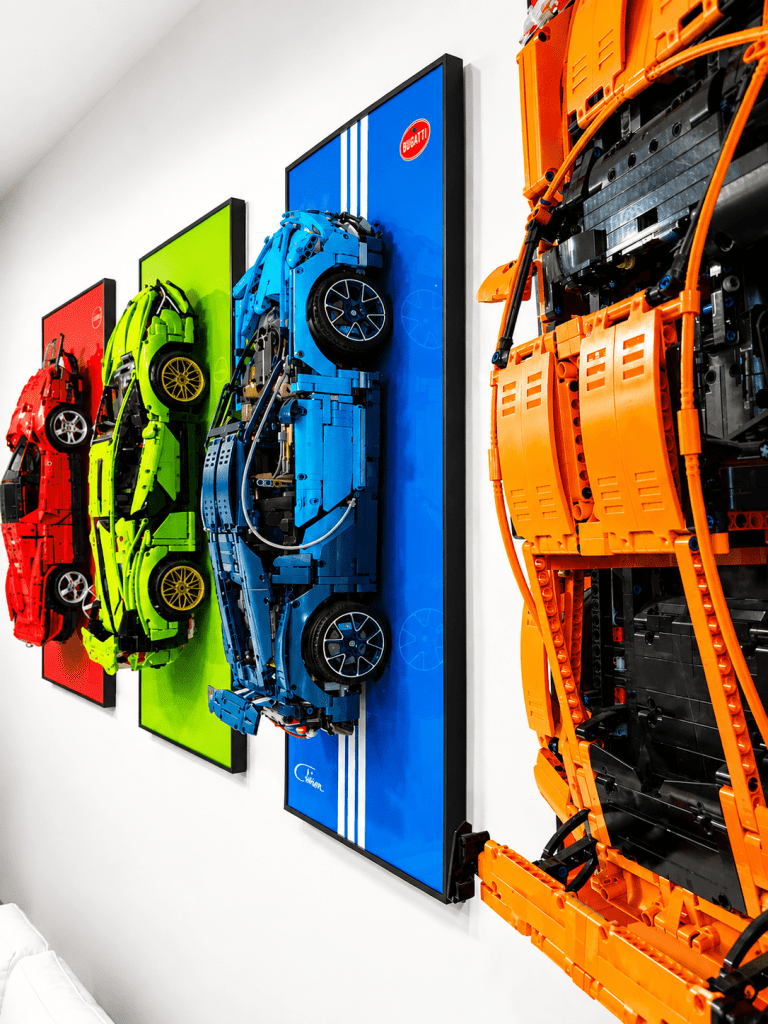 Finished LEGO Technic wall art installation with five cars on dark painted wall