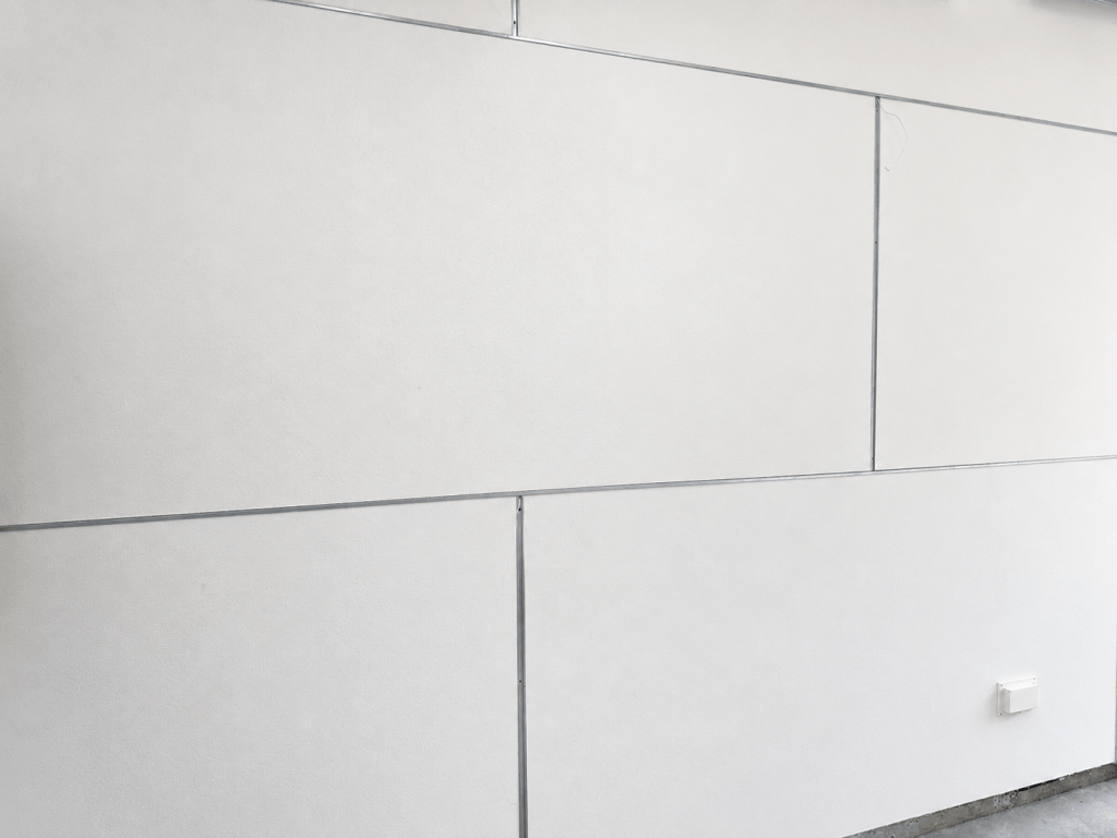 A close-up view of a light gray textured wall with large rectangular panels and visible seams.