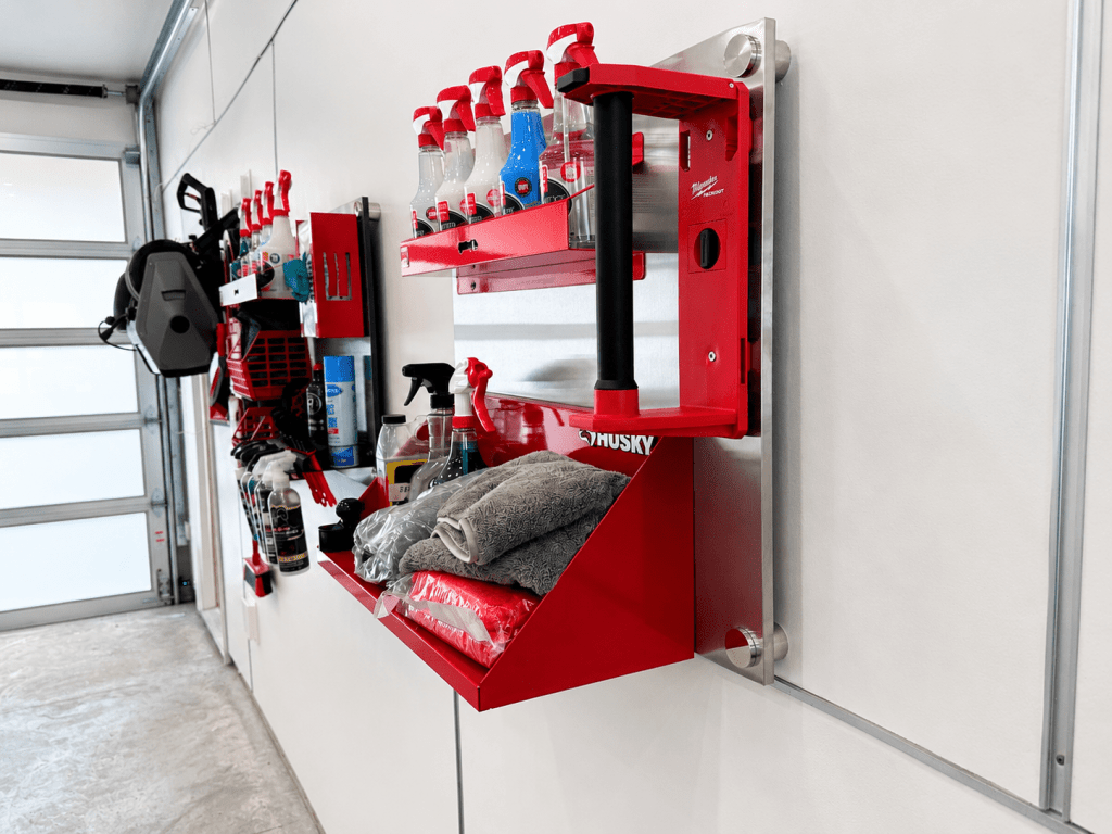 A well-organized garage wall featuring red storage shelves with various cleaning products, towels, and a tool holder, against a clean white background.