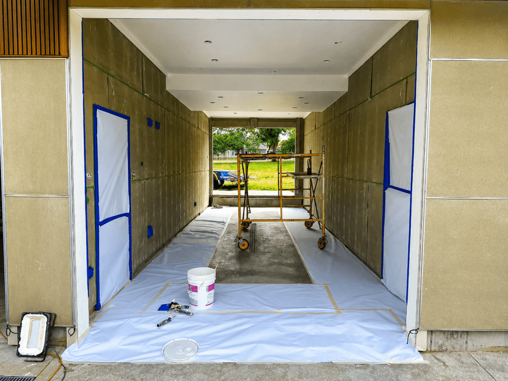 A construction area featuring a partially finished room with exposed walls, scaffolding in the middle, and a clean floor covered with protective plastic sheeting.