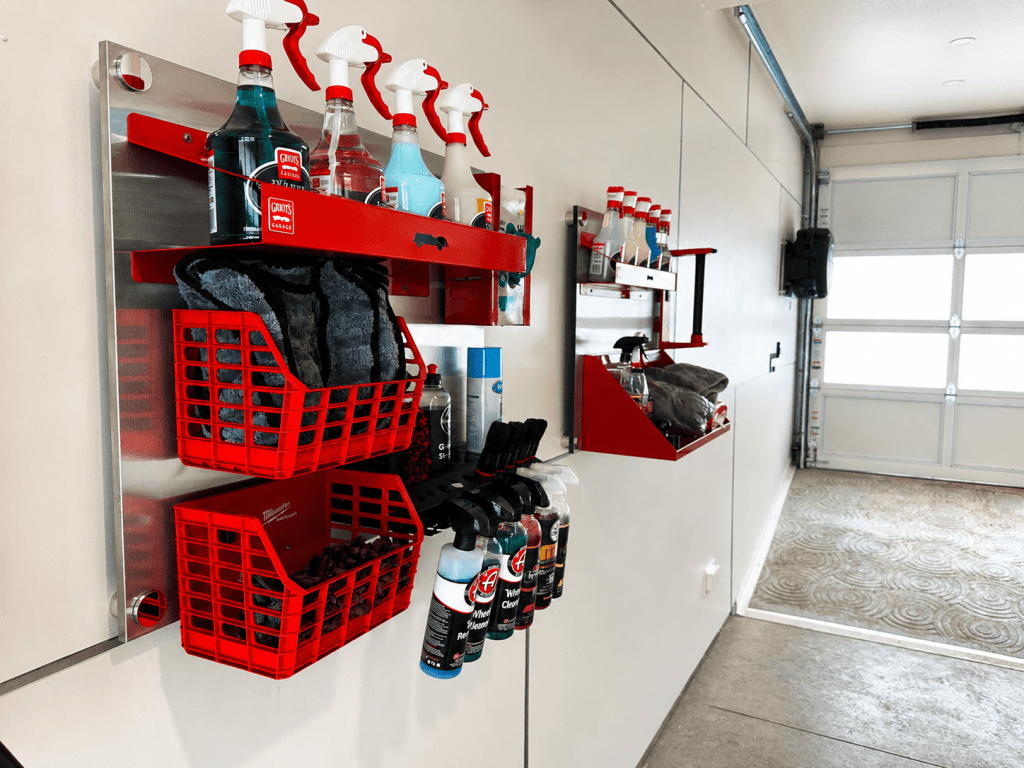 Wall-mounted storage system in a garage, featuring red baskets and various cleaning supplies including spray bottles and microfiber cloths.